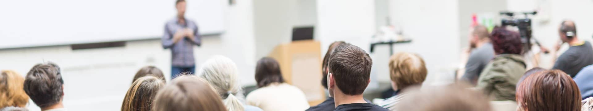 Unterschiedliche Studenten in einer Universität hören einer Person zu, die einen Vortrag hält.