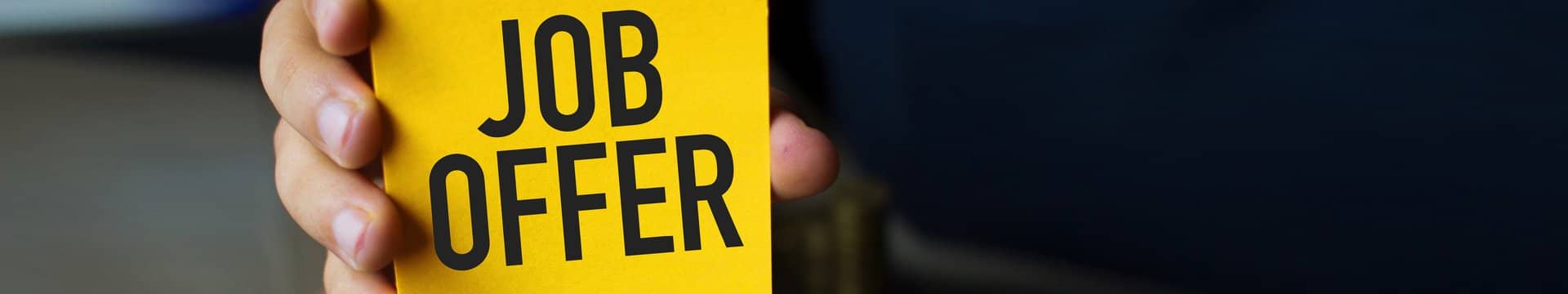 Eine Hand, die ein gelbes Schild zeigt mit der schwarzen Aufschrift "JOB OFFER".